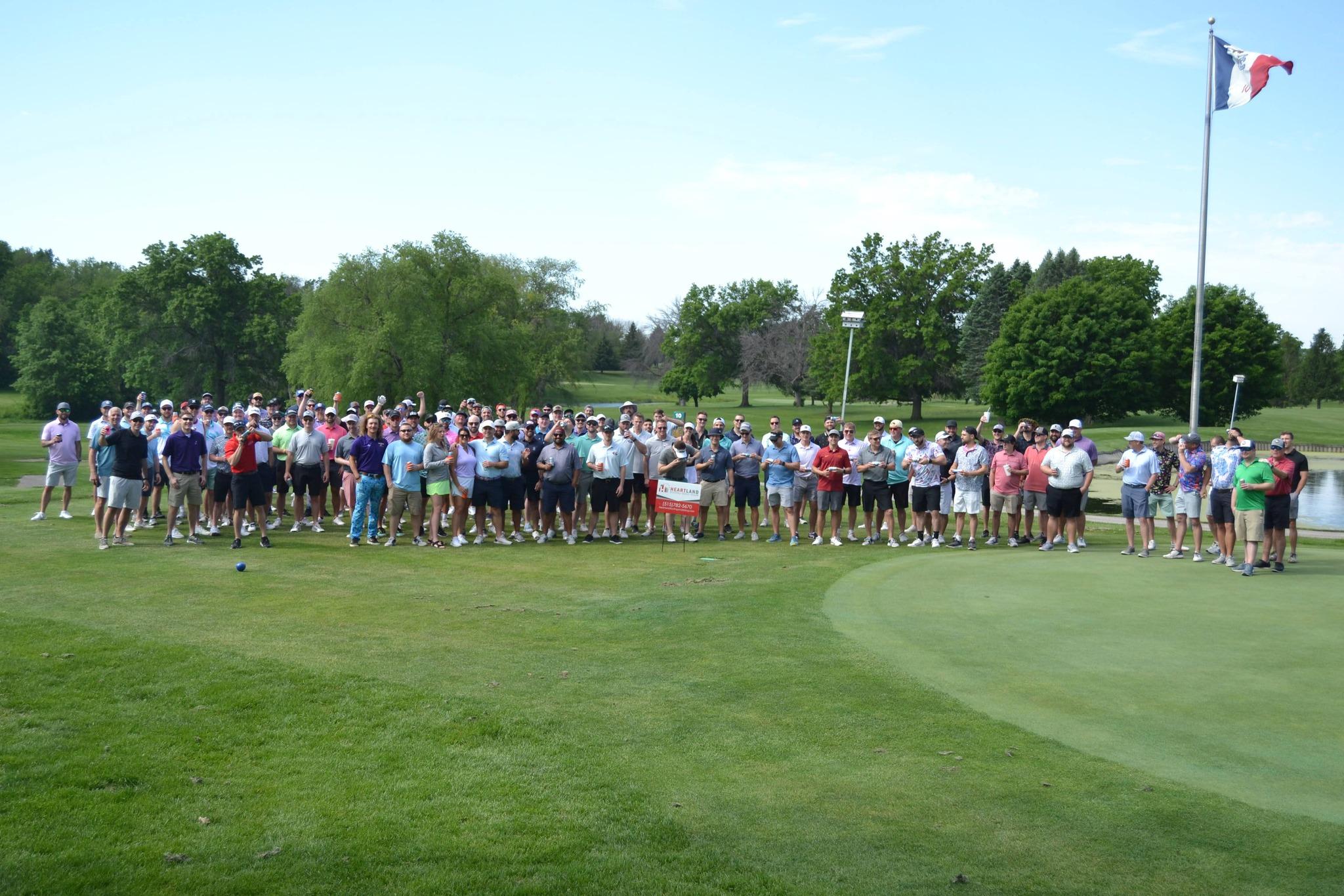 Pop-A-Top Classic golfers gathered on the green for a group photo, Iowa state flag flying