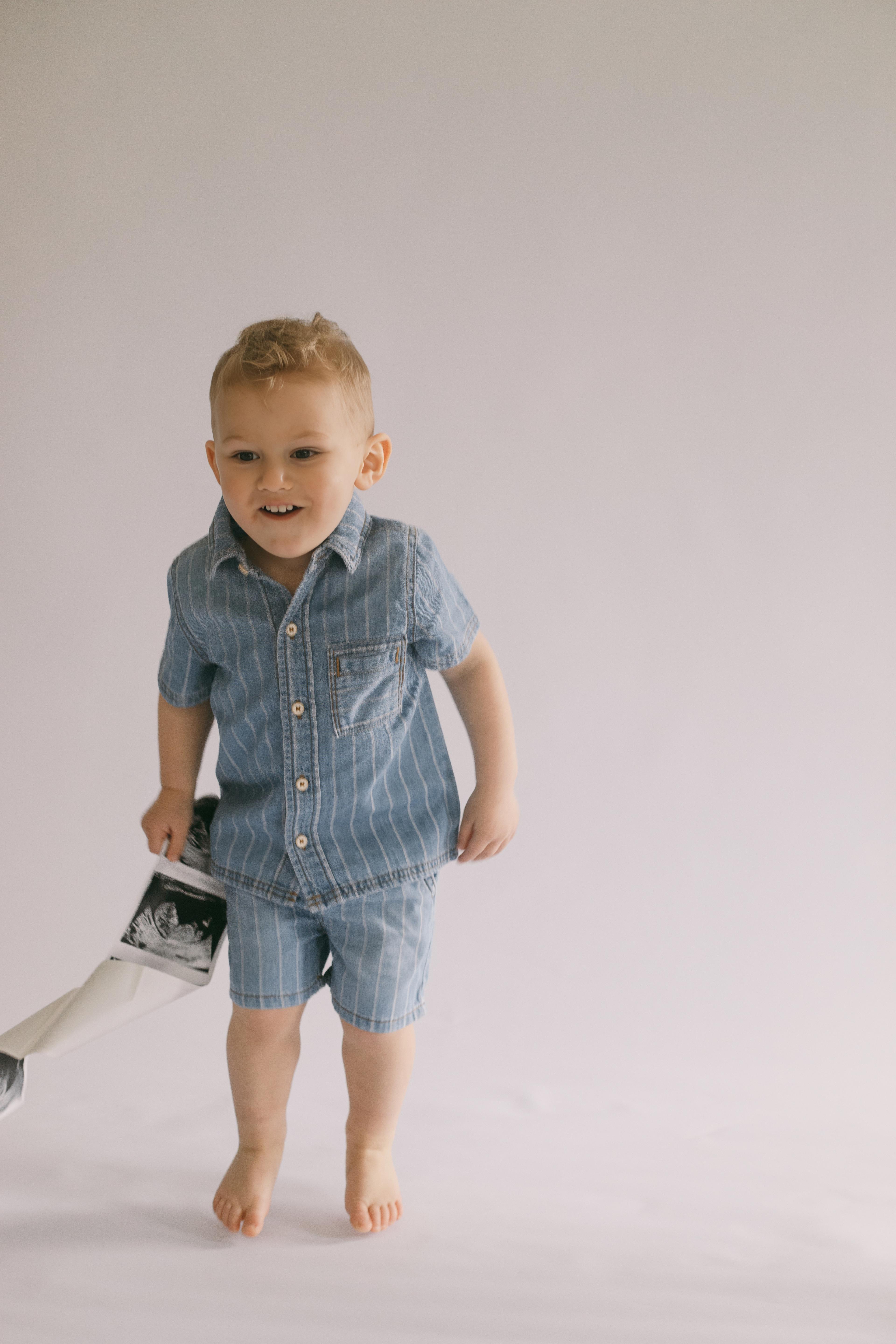 The Schellings' son walking and smiling, holding a sonogram photo of his future sibling